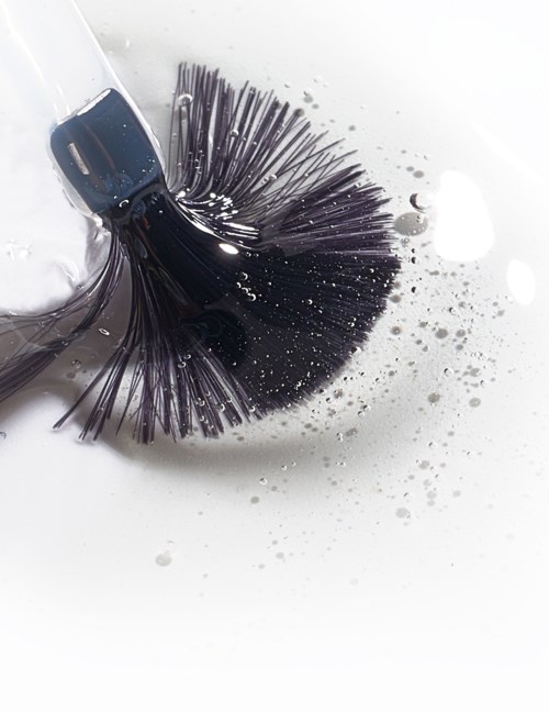A black hairbrush is in soapy water, with bubbles and water splashes around it.