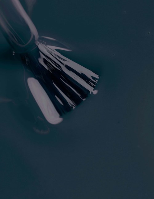 A paintbrush is touching blue paint, creating a streak. The background is dark and solid.