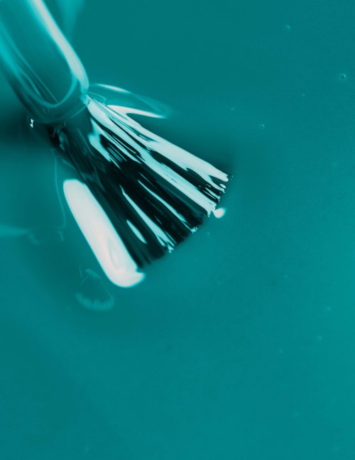 A brush is shown, touching a smooth surface with a shiny reflection, suggesting cleaning or painting activity.