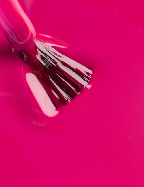Pink paint is being spread or mixed with a brush. The surface is bright pink and glossy.