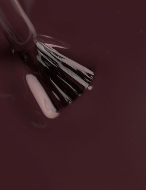 A makeup brush with pink lipstick and dark red nail polish in background.