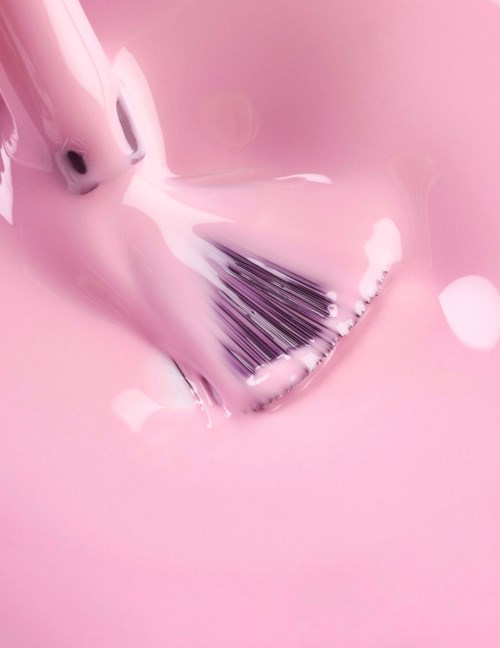 En makeupborste rengörs i rosa vätska, vilket skapar skum och stänk.