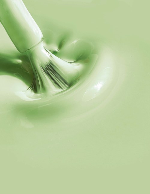 A brush is mixing green paint smoothly in a container.