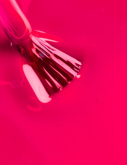 En metallisk borste med svarta borsthår på en klar rosa bakgrund.