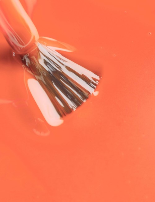 A paintbrush is dipped in orange paint on a surface.