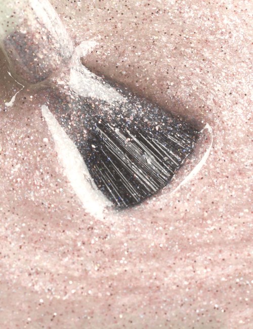 En makeupbørste fordeler pink glitter på huden. Nærbillede af glitrende og blød tekstur.