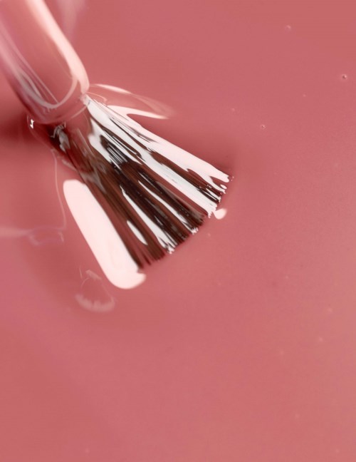 A silver brush is on pink surface, with some liquid around. The image is close-up focusing on the brush and liquid.