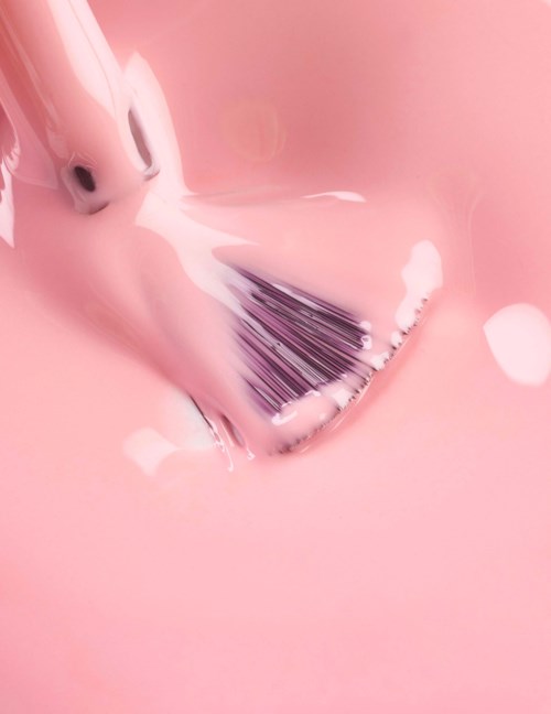 En makeupborste doppas i rosa vätska, vilket skapar bubblor och skum runt den.