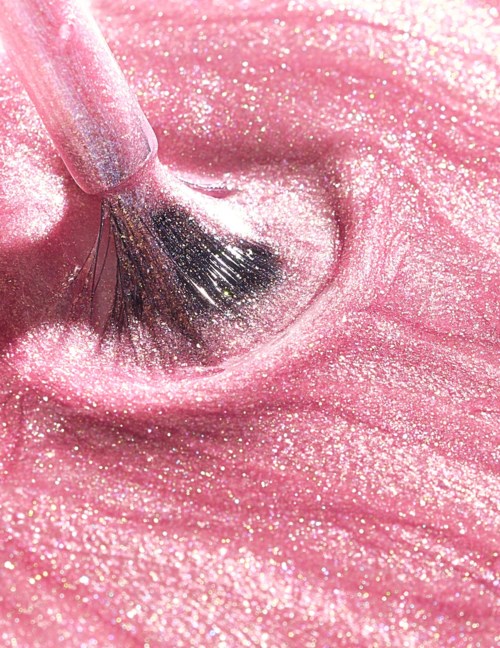 A pink makeup brush is spreading glittery pink product on skin.