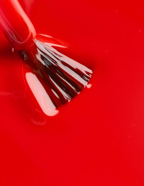 A brush is painting a red surface, creating paint strokes and splashes.
