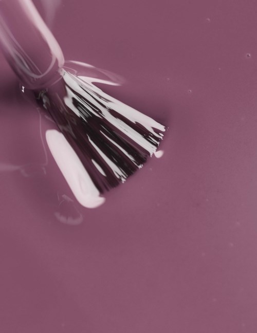 En malerpensel er dyppet i rosa maling, og den lager penselstrøk på en rosa overflate.