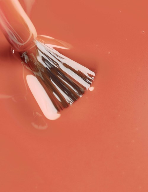 A paintbrush is spreading white paint on a pink surface.