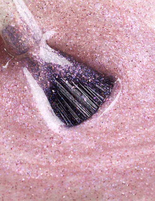 A nail with shiny pink glitter polish and a dark, glittery triangle design.