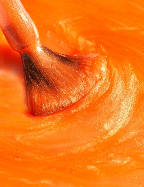 A brush mixes orange paint or sauce smoothly, creating a swirling pattern.