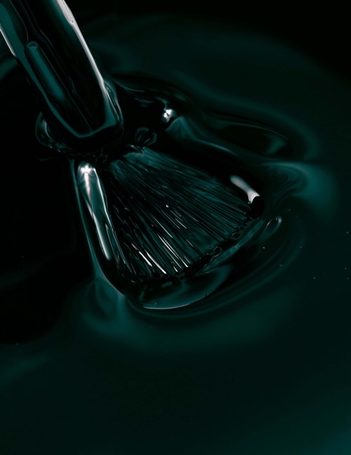 Black liquid being stirred with a brush, creating flowing patterns and reflections.