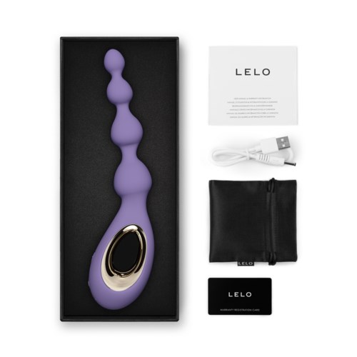 A purple, curved, sensory massager with a gold accent, along with a USB charger, instruction card, pouch, and card in box.