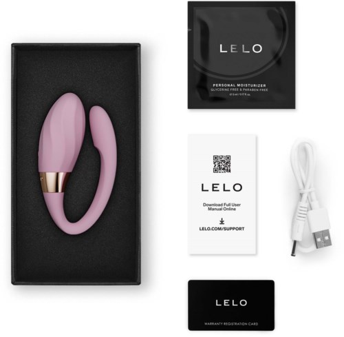 Rosa silikon vibrator med gullfarget ring i svart eske, sammen med brukerhåndbok, ladeledning, garantikort og produktets emballasje.