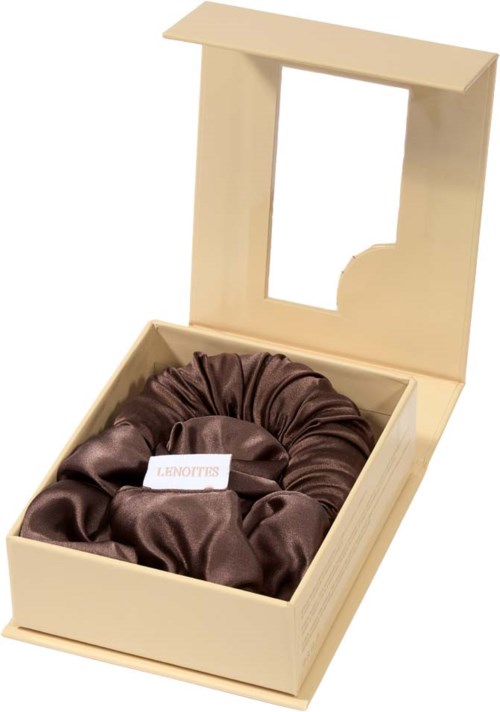 En beige æske med et klart vindue indeholder en brun satinskrans. Æsken er åben og ser elegant ud.