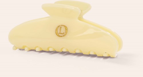 En liten, kremfarget hårklype med en gullfarget L-logo og teksturerte tenner i bunnen.