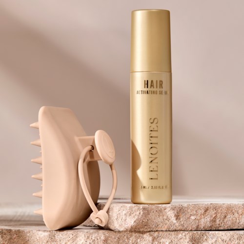 A beige hairbrush with a strap and a gold can of L'Occitane hair spray on a stone surface.