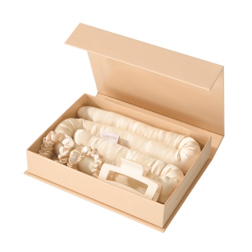 Ein cremefarbener Karton mit einem langen, aufgerollten Stoff und einem kleinen Gerät darin, vermutlich für Hautpflege oder Schönheit.
