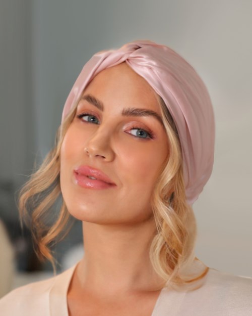 A woman wears a pink headscarf, has blonde hair, and a soft smile. She looks calm and confident.