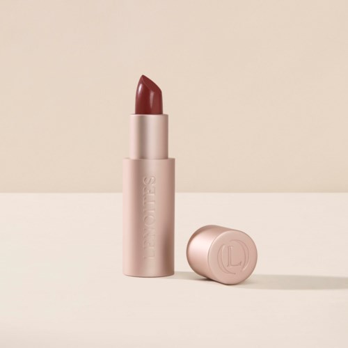 En läppstift i ett rosa fodral, med lock off, som visar en rödbrun färg på en beige bakgrund.