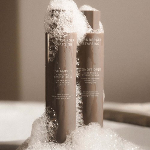 Two shampoo and conditioner bottles are covered in foam, standing upright. The bottles are labeled with product details.
