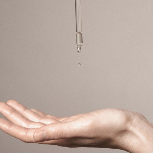 En hand fångar en droppe vätska från ett pipett mot en enkel bakgrund.