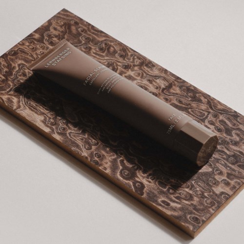 A lotion tube placed on a textured, dark brown rectangular surface with a white background.