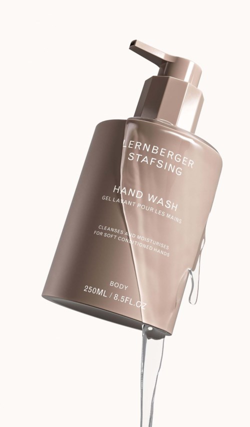 Een beige handzeepdispenser met pomp, gelabeld met merk en instructies, rechtopstaand.