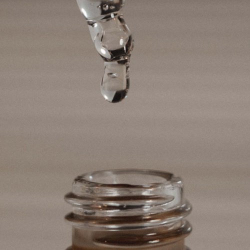 A water droplet is falling into a small glass bottle, creating ripples inside.