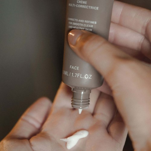 A hand dispenses cream from a tube onto the palm. The tube is gray and has instructions and text on it.