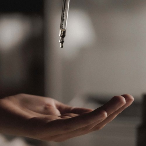 A hand under a dropper releasing liquid in a clinical setting.