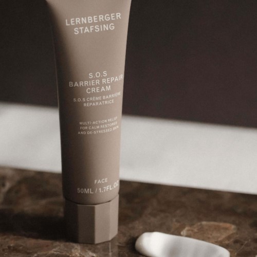 A tube of Lederberger SOS Barrier Repair Cream on a dark surface, with text and a small white object nearby.