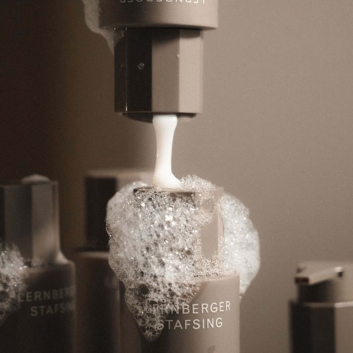 A soap dispenser releases foam soap into a container, with other soap bottles nearby.