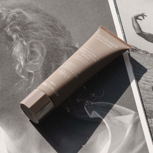 A tube of face cream lies on a black-and-white magazine page near a person's curly hair and an artistic sketch.