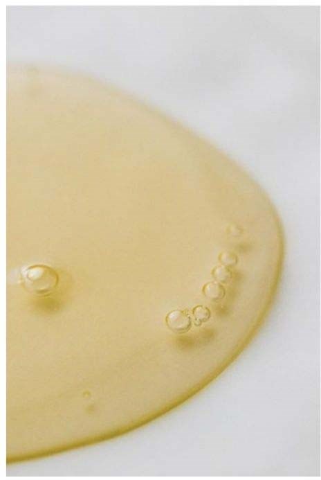 En gulaktig væske med bobler på hvit overflate, sannsynligvis olje eller sirup, vist i nært bilde.