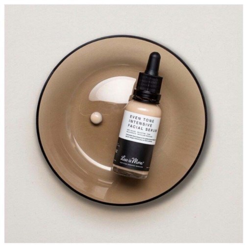 A facial serum bottle with a dropper, placed inside a beige bowl with some serum liquid and a small white pill.