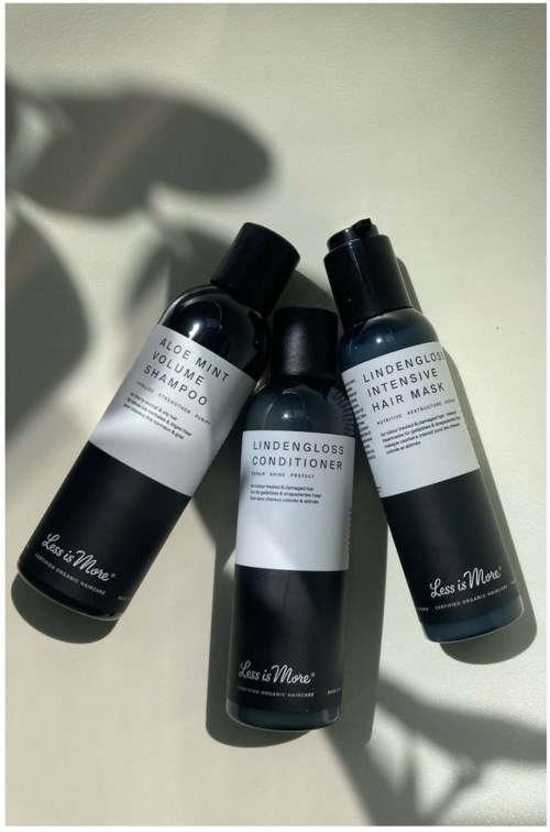 Tre svarte flasker med hårpleieprodukter med hvite etiketter står på en hvit overflate og kaster skygger.