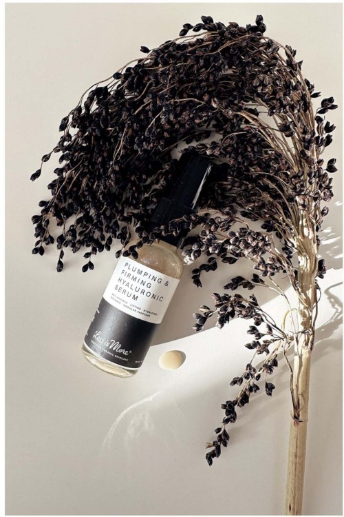 A skincare bottle is placed beside a bunch of dark lavender flowers on a white surface.