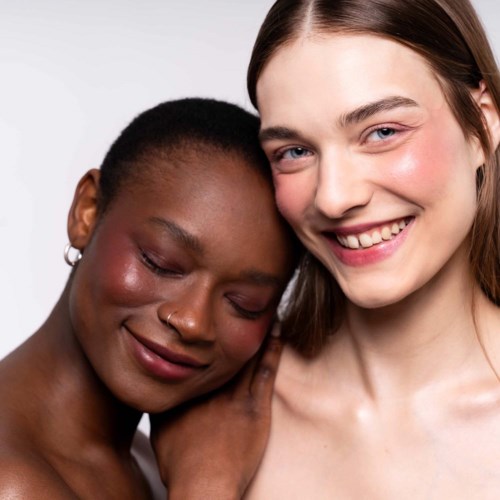 Twee vrouwen staan dicht bij elkaar, glimlachen zacht, tonen vriendschap en comfort.