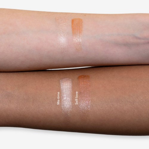 Swatches of two different makeup products are shown on two arms. One arm has an orange-brown shade, the other a lighter, silvery shade.