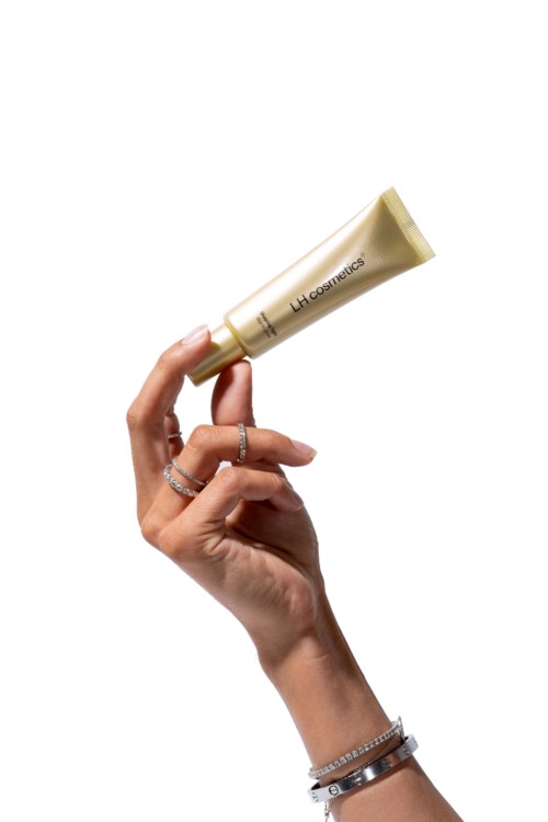 En hand håller i en beige tub med märket "LHE Cosmetics" på.