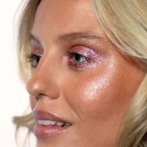 Close-up of a woman's face with shiny makeup, highlighting her eye, cheek, and lips.