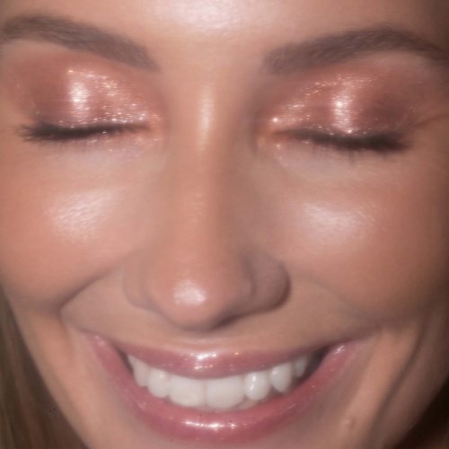 A woman with sparkly eyeshadow, smiling with closed eyes and showing teeth.