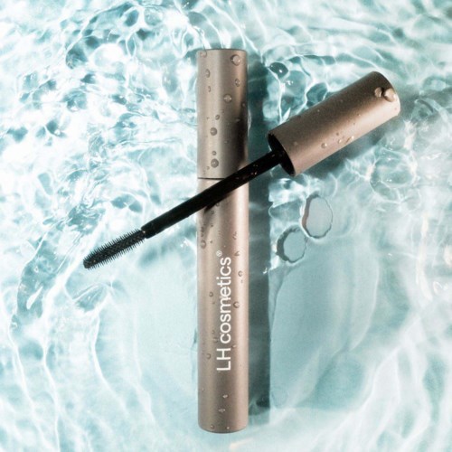 Een mascara-tube drijft in water met de borstel uitgestoken, waterdruppels op de verpakking.