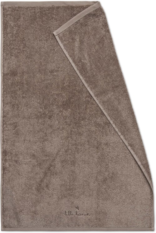 En brun, mjuk handduk med en del som är vikt över sig själv. Handduken har en liten logga eller text längst ner.