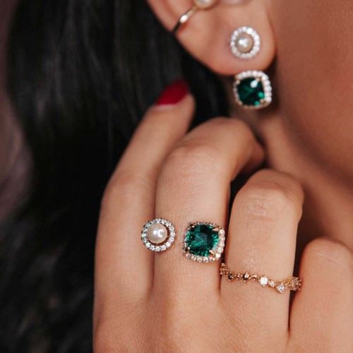 Close-up of hand showing rings with a pearl, green gemstone, and small diamonds, and a matching earring.