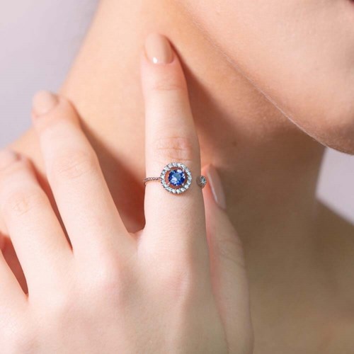 A hand with a ring featuring a large blue gemstone surrounded by smaller diamonds.